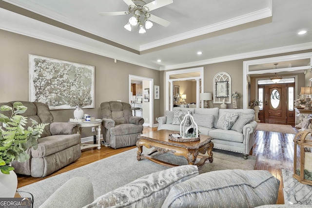 living room with hardwood / wood-style floors, a raised ceiling, ceiling fan, and ornamental molding