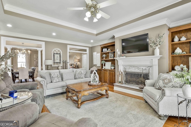 living room with ceiling fan with notable chandelier, light hardwood / wood-style flooring, built in shelves, ornate columns, and ornamental molding