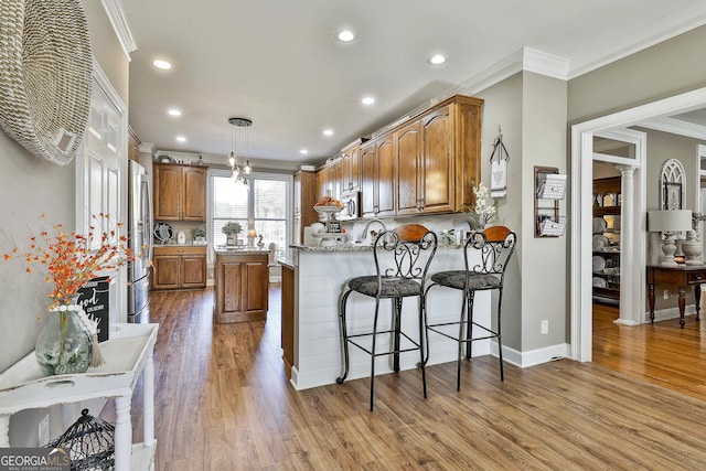 kitchen with light stone counters, ornamental molding, stainless steel appliances, hardwood / wood-style floors, and hanging light fixtures