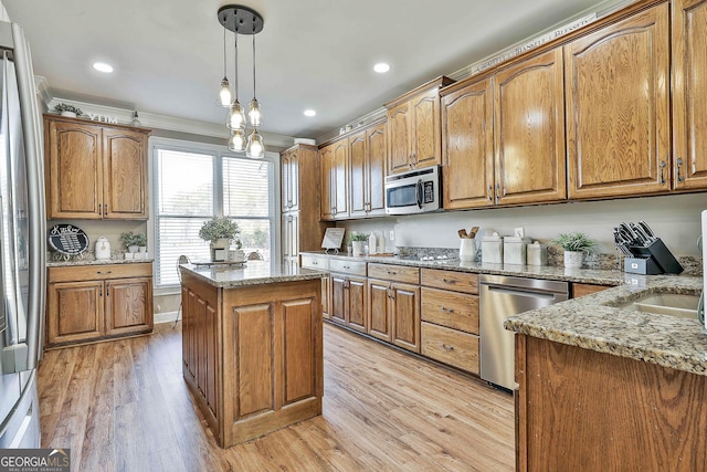 kitchen with appliances with stainless steel finishes, crown molding, decorative light fixtures, light hardwood / wood-style flooring, and a kitchen island