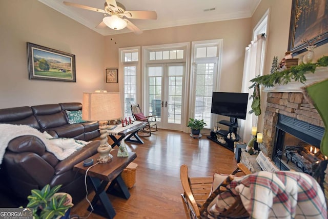 living room featuring crown molding, light hardwood / wood-style flooring, ceiling fan, a stone fireplace, and french doors