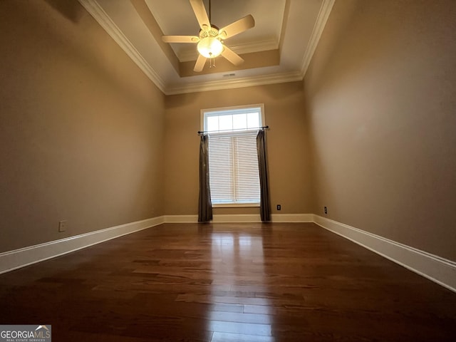 empty room with ceiling fan, a tray ceiling, dark hardwood / wood-style flooring, and ornamental molding