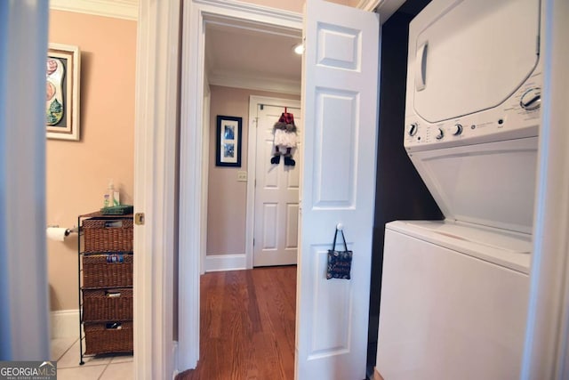 laundry room featuring stacked washer / dryer, crown molding, and wood-type flooring