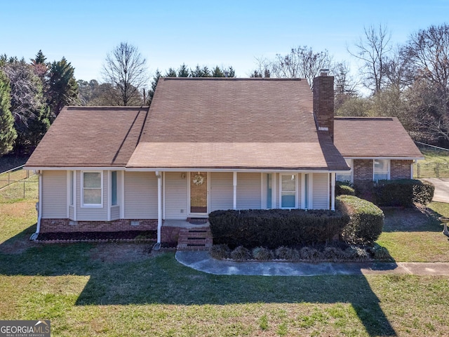 view of front facade featuring a front yard, covered porch, brick siding, and a chimney