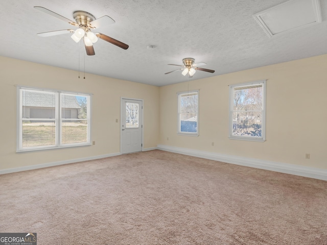 empty room with light colored carpet, attic access, a ceiling fan, a textured ceiling, and baseboards