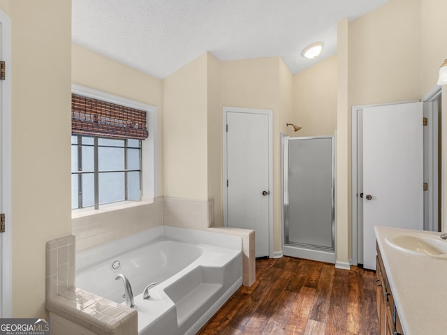 bathroom with a textured ceiling, wood finished floors, vanity, a bath, and a stall shower