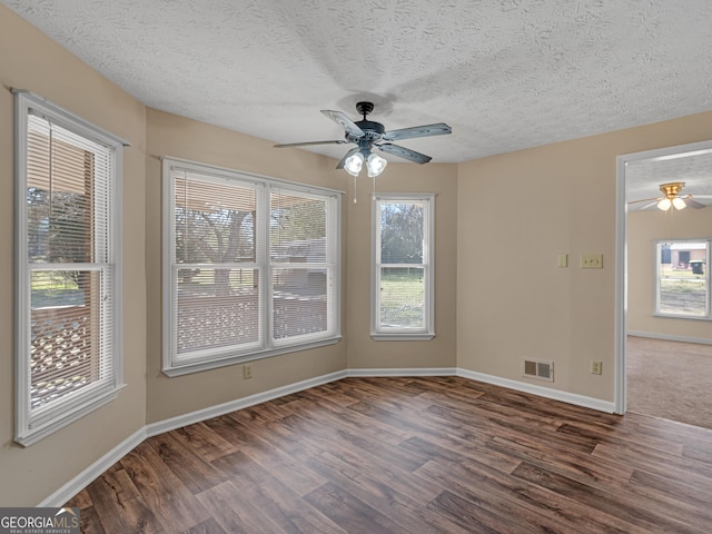 unfurnished room featuring visible vents, dark wood-type flooring, a ceiling fan, a textured ceiling, and baseboards