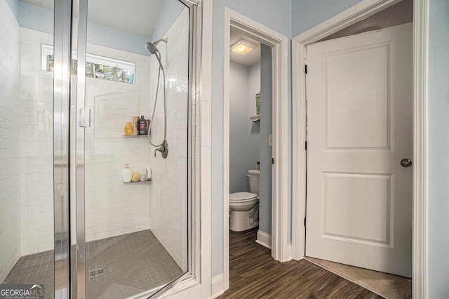 bathroom featuring toilet, a shower with door, and wood-type flooring