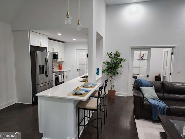 kitchen featuring white cabinetry, hanging light fixtures, stainless steel appliances, dark hardwood / wood-style flooring, and a breakfast bar area