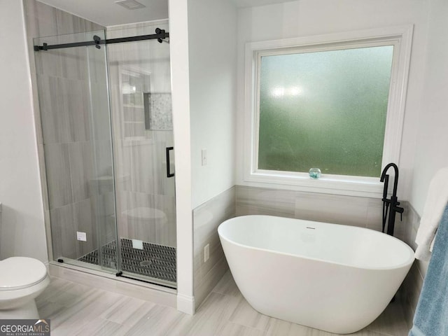 bathroom featuring toilet, tile walls, and plus walk in shower