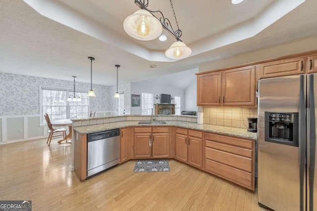 kitchen featuring a tray ceiling, decorative light fixtures, light hardwood / wood-style floors, kitchen peninsula, and stainless steel appliances