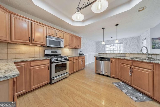 kitchen featuring sink, hanging light fixtures, light wood-type flooring, appliances with stainless steel finishes, and a tray ceiling