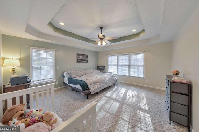 carpeted bedroom with ceiling fan, a tray ceiling, and multiple windows