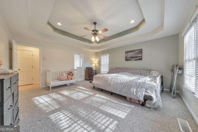 bedroom with light carpet, a raised ceiling, and ceiling fan