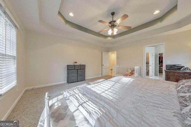 unfurnished bedroom with light carpet, a tray ceiling, a walk in closet, and ceiling fan