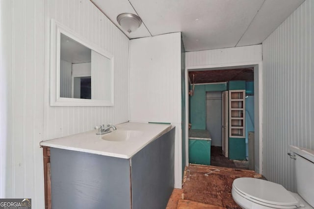 bathroom with vanity, wood walls, and toilet