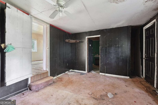 empty room featuring ceiling fan and wooden walls