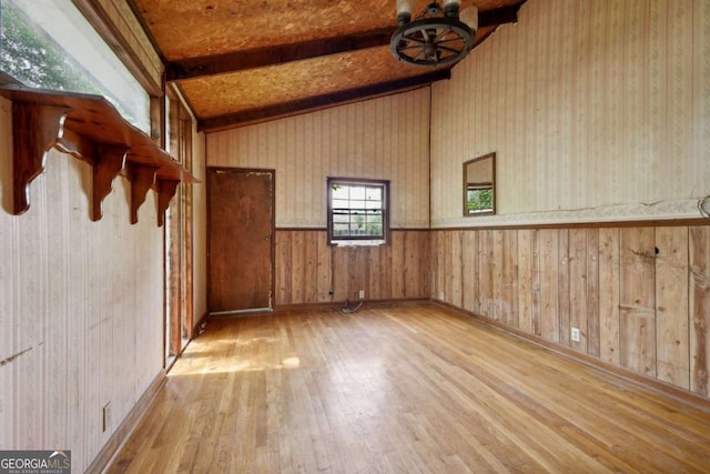 empty room featuring vaulted ceiling with beams, light wood-type flooring, and wood walls