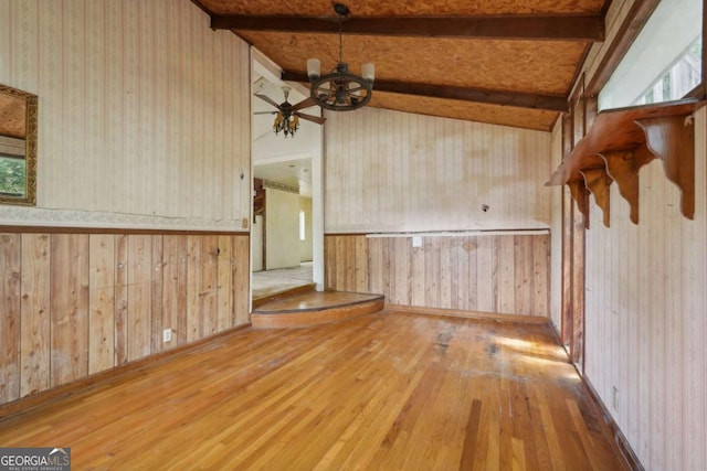 empty room with hardwood / wood-style floors, wood walls, ceiling fan with notable chandelier, beamed ceiling, and a healthy amount of sunlight