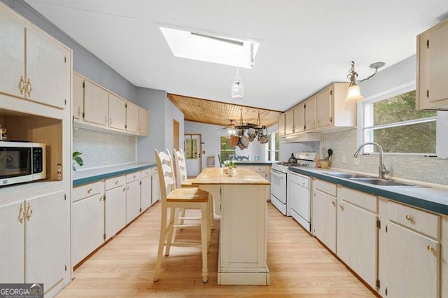 kitchen featuring a breakfast bar, a center island, white appliances, sink, and light wood-type flooring