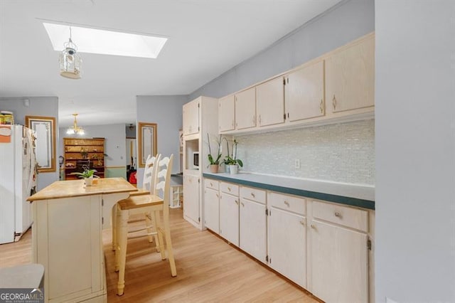 kitchen featuring light wood-type flooring, a skylight, white refrigerator, decorative light fixtures, and a kitchen island