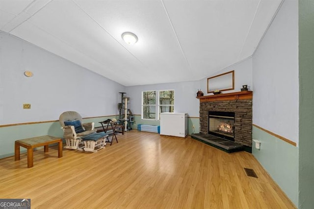 living area featuring a stone fireplace, lofted ceiling, and light hardwood / wood-style flooring