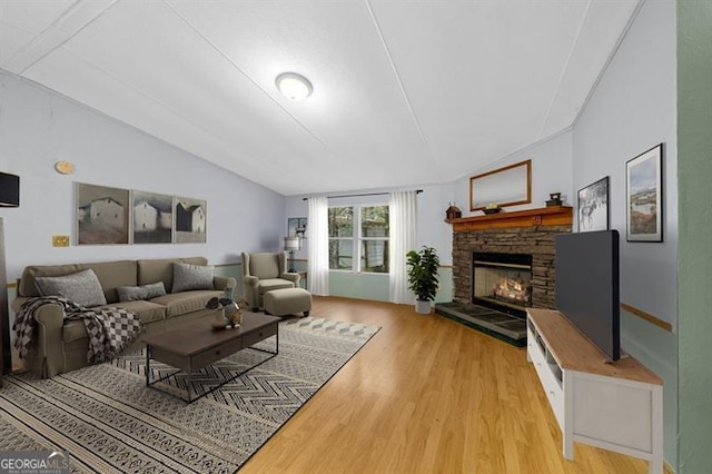 living room featuring a stone fireplace, light hardwood / wood-style floors, and lofted ceiling