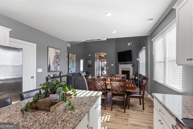 kitchen featuring white cabinets, light hardwood / wood-style flooring, stainless steel refrigerator, and light stone counters