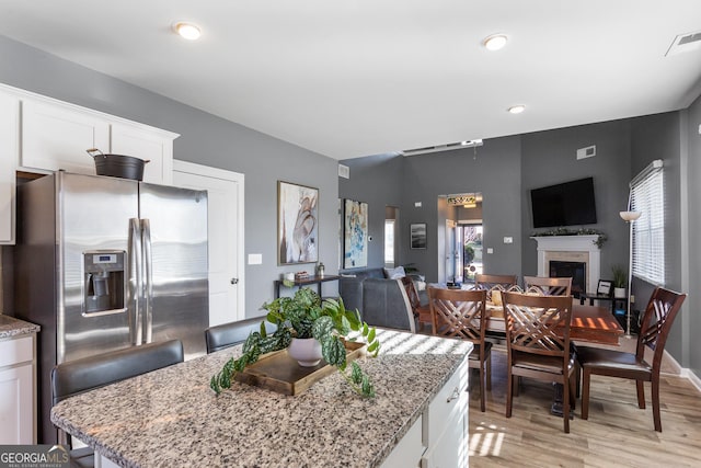 kitchen featuring stainless steel fridge, light stone counters, white cabinetry, and light hardwood / wood-style flooring