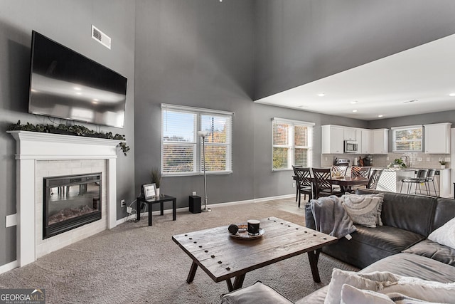 living room featuring light carpet, a high ceiling, and a tiled fireplace