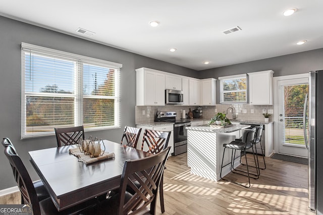 kitchen with white cabinets, light hardwood / wood-style floors, stainless steel appliances, and a wealth of natural light