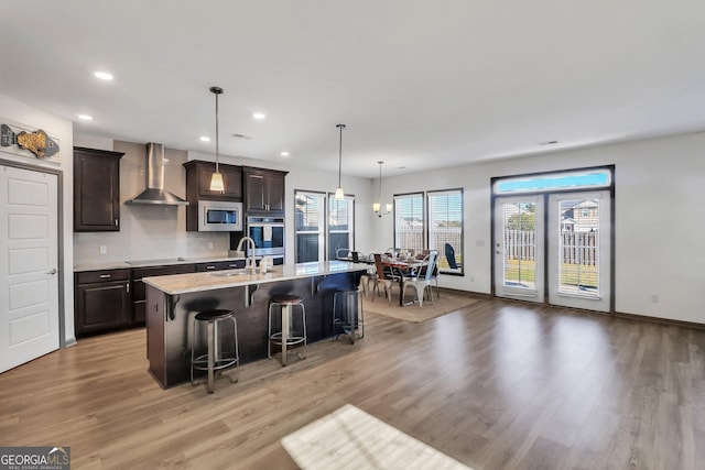 kitchen featuring a kitchen bar, appliances with stainless steel finishes, wall chimney exhaust hood, light hardwood / wood-style floors, and an island with sink