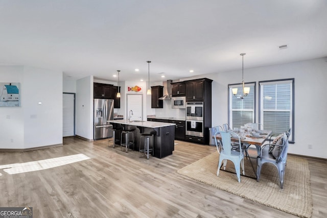 kitchen with wall chimney exhaust hood, hanging light fixtures, stainless steel appliances, a breakfast bar, and a center island with sink