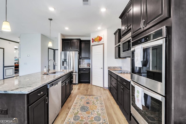 kitchen featuring stainless steel appliances, a kitchen island with sink, sink, light hardwood / wood-style floors, and hanging light fixtures