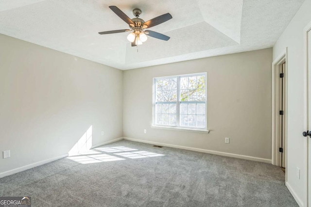 empty room with a raised ceiling, light carpet, ceiling fan, and a textured ceiling