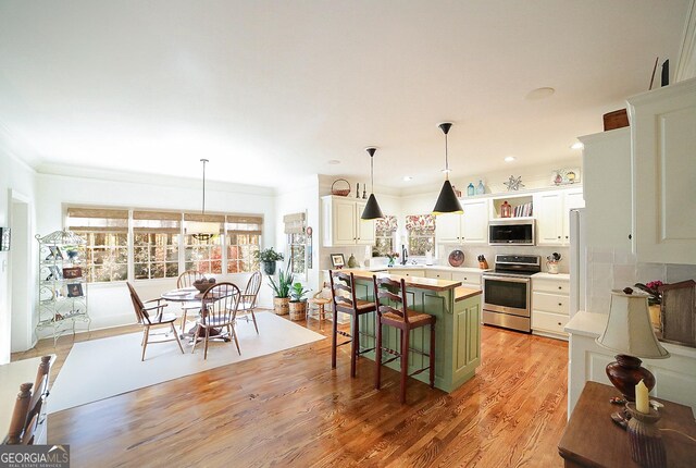 kitchen with pendant lighting, white cabinets, light wood-type flooring, appliances with stainless steel finishes, and a kitchen island