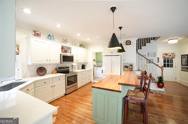 kitchen with white cabinets, stainless steel appliances, hanging light fixtures, and butcher block counters