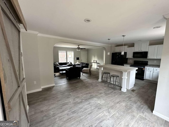 kitchen with crown molding, a kitchen bar, arched walkways, light wood-style floors, and black appliances