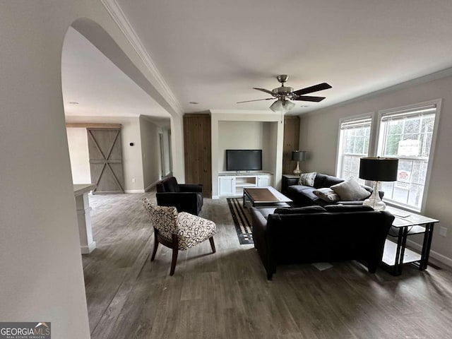 living area featuring ornamental molding, dark wood-type flooring, baseboards, arched walkways, and ceiling fan