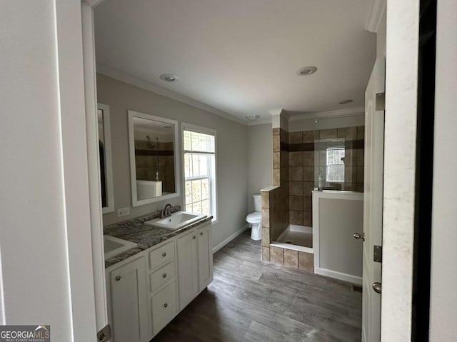 bathroom with ornamental molding, vanity, tiled shower, hardwood / wood-style flooring, and toilet