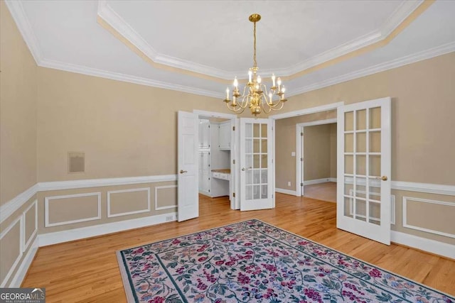 dining area with ornamental molding, french doors, wood-type flooring, and an inviting chandelier