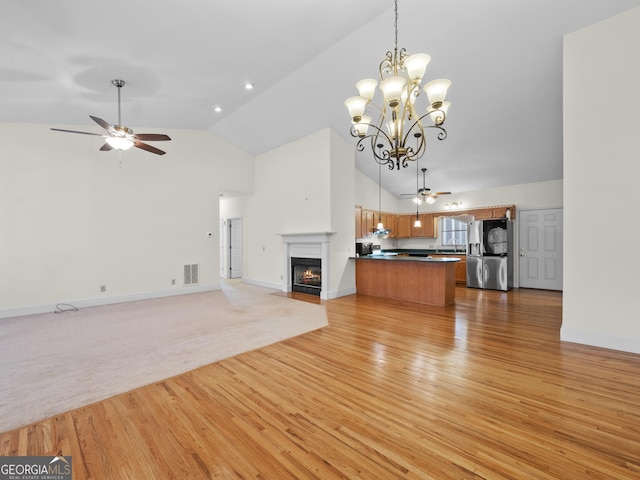 unfurnished living room with high vaulted ceiling, ceiling fan with notable chandelier, and light wood-type flooring