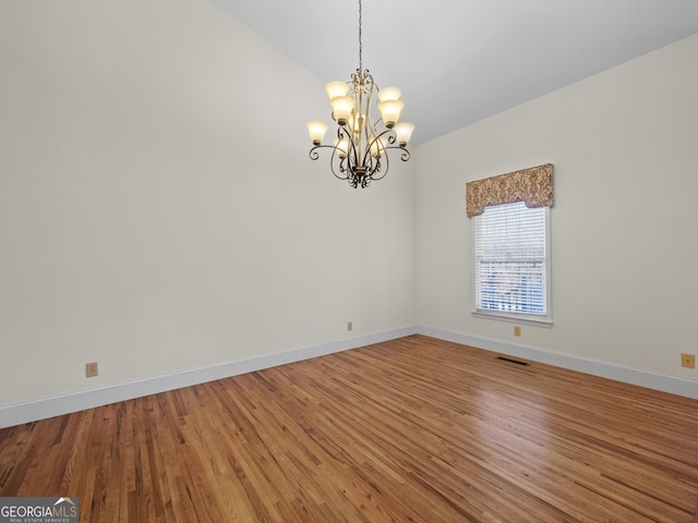 spare room with hardwood / wood-style flooring and a notable chandelier