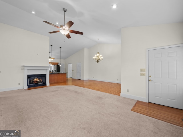 unfurnished living room with ceiling fan with notable chandelier, high vaulted ceiling, and light hardwood / wood-style flooring