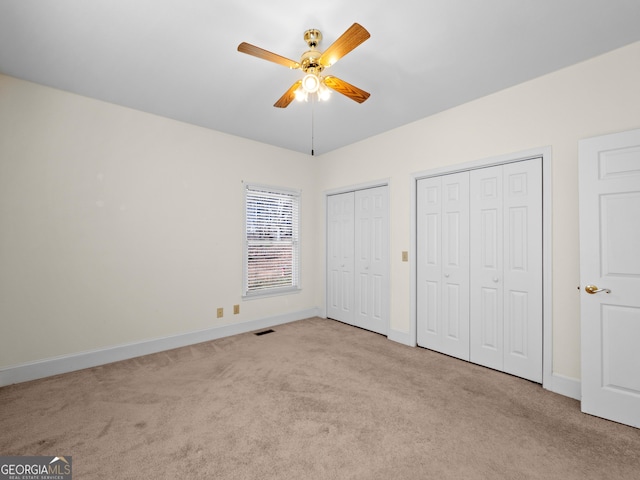 unfurnished bedroom featuring light colored carpet, ceiling fan, and multiple closets