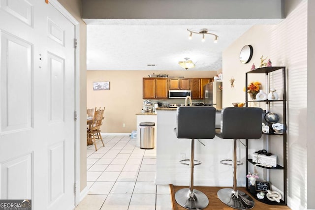 kitchen featuring a kitchen breakfast bar, light tile patterned floors, a textured ceiling, and appliances with stainless steel finishes