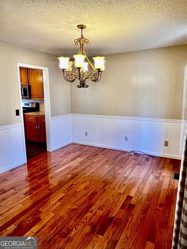 unfurnished dining area featuring a textured ceiling, a chandelier, and dark hardwood / wood-style floors