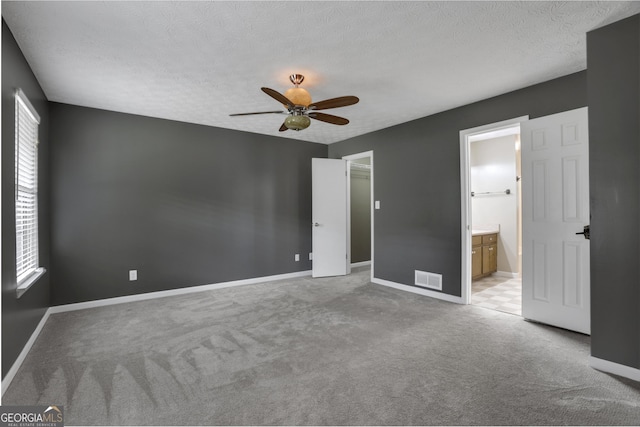 unfurnished bedroom featuring ceiling fan, a textured ceiling, connected bathroom, and light carpet