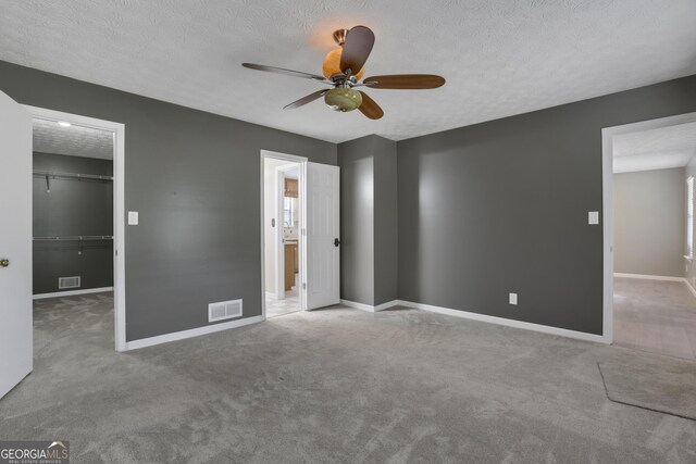 unfurnished bedroom with a spacious closet, ceiling fan, carpet floors, a textured ceiling, and a closet