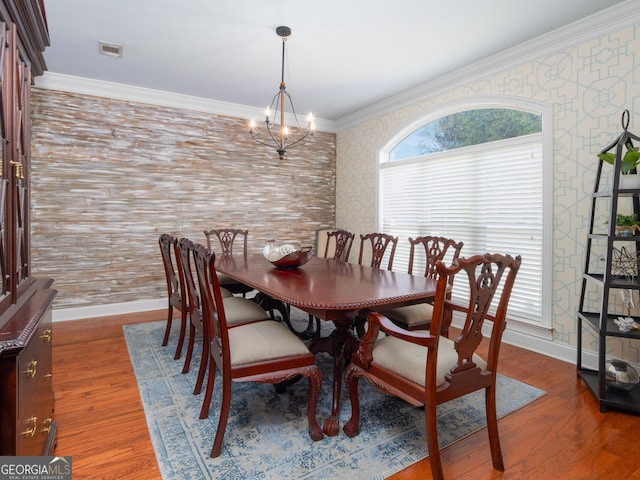 dining area with ornamental molding, a notable chandelier, and hardwood / wood-style flooring